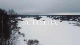 Зимняя панорама реки Мологи и заснеженного берега в Устюжне, вид сверху с размытым горизонтом и наложенной надписью «УСТЮЖНА».