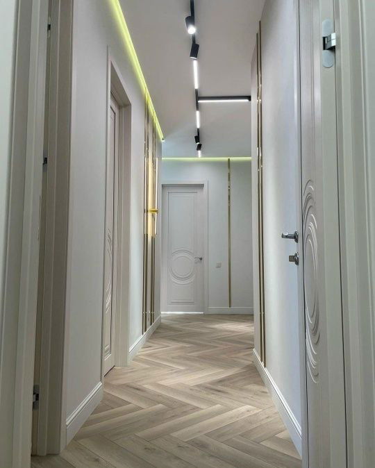 Длинный коридор с установленными дверями Дивайн 6, светлый паркет «ёлочка», потолочные светильники и декоративная строчная подсветка по периметру.