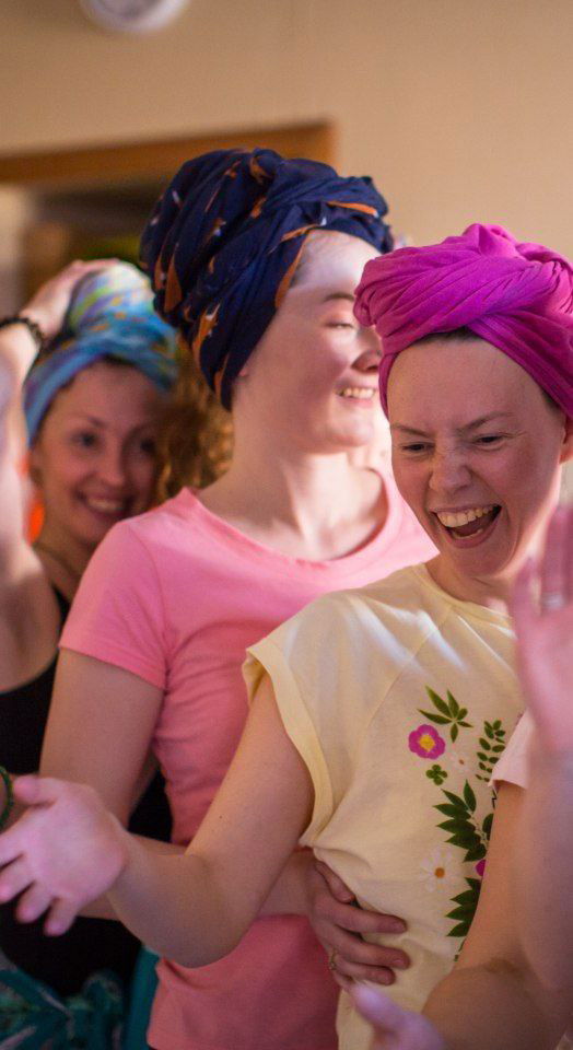 Участницы занятия в повязках на голове смеются и двигаются вместе, выражая лёгкость, эмоциональную поддержку и групповой контакт.