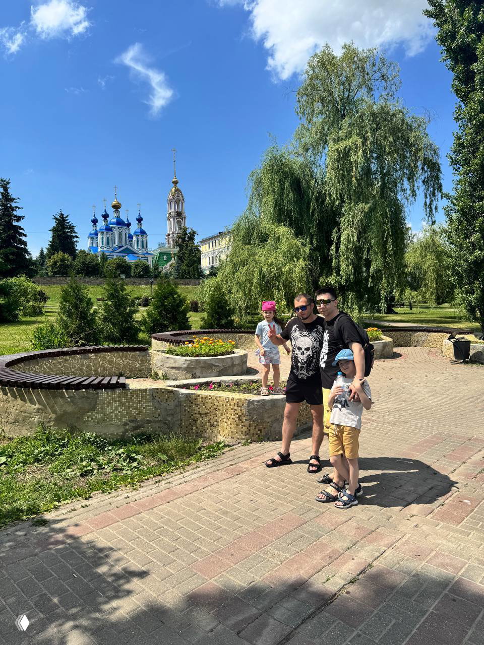 Семья с двумя детьми на прогулке в парке на фоне синей купольной церкви и зелёных насаждений: городской пейзаж и отдых на природе.