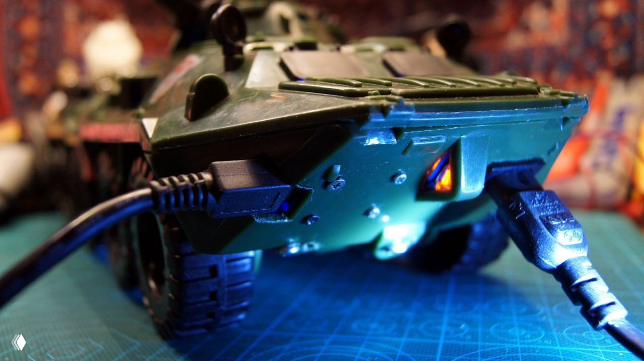 Нижняя сторона игрушечного БТР с подключёнными кабелями: видны USB-разъёмы и подсветка, показана коммутация питания и интерфейсов мини-консоли для ретро-игр.