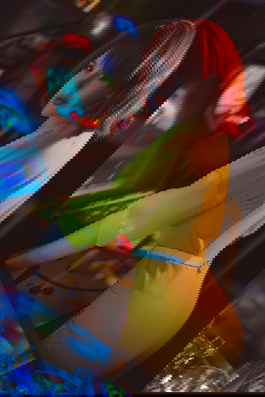 Боковой ракурс косплеера Эйприл О'Нил в жёлтом костюме у аркадного автомата: динамичная поза, неоновое освещение и элементы ретро‑игр на заднем плане.