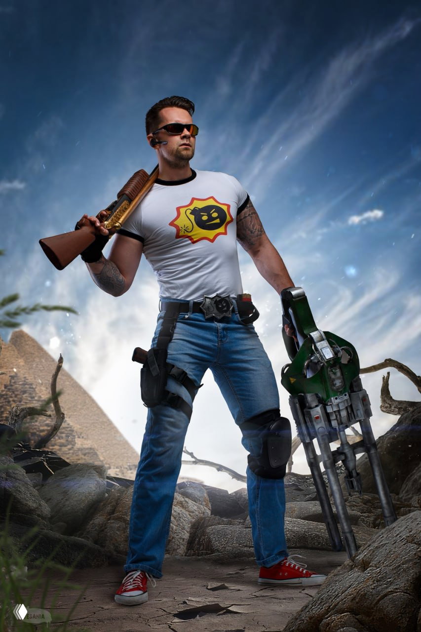 Портрет косплеера Serious Sam: полный рост в джинсах и кедах, с ружьём через плечо и большим оружием в руках на эпическом небе.