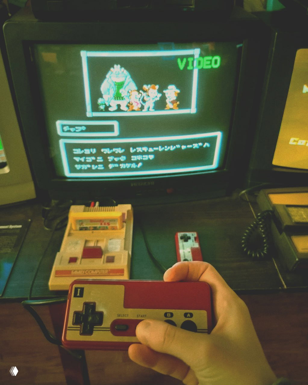 Крупный план ретро-консоли Sega Dreamcast и двух контроллеров на фоне включённого монитора с яркой заставкой игры.