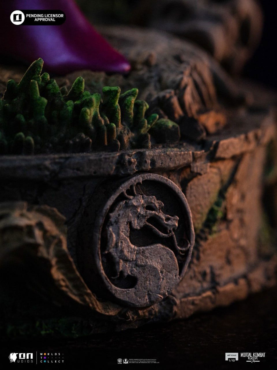 Крупный план основания диорамы со знаком Mortal Kombat: фактура камня, мох и рельефный логотип дракона в фокусе.