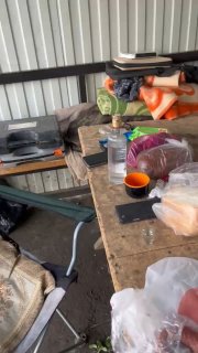 Скромный рыбацкий лагерь в навесе: стол с продуктами, кружкой, бутылкой воды и снаряжением — бытовка/навес у водоёма после рыбалки.