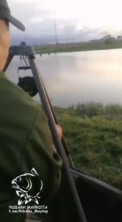 Вертикальный кадр: вид на спокойную заводь и рыболова на берегу, пасмурная погода и отражение неба — фото из отчёта 13.04, канал РЫБАКИ МАЙКОПА.