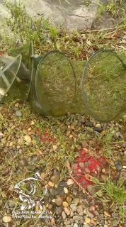 Вертикальное фото берега водоёма Лесной Остров с садком и снастями на гальке, заметен фирменный логотип «РЫБАКИ МАЙКОПА».