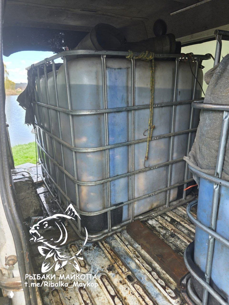 Крупный план второго еврокуба в машине у водоёма: подготовка ёмкостей для слива воды и вид на береговую линию озера на заднем плане.