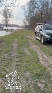 Автомобиль припаркован на грунтовой дорожке у пруда, вдоль берега видны рыбаки и техника для подъезда к месту ловли — типичный подъезд к платнику.