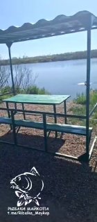 Беседка с металлической крышей, столом и скамьями на берегу Морозовских прудов, вид на водоём и прибрежную растительность, логотип канала
