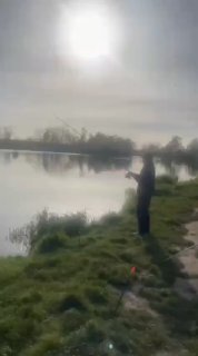 Силуэт рыбака на фоне яркого солнца над водоёмом: отражение в воде, дальний берег с деревьями и фирменный водяной знак канала.