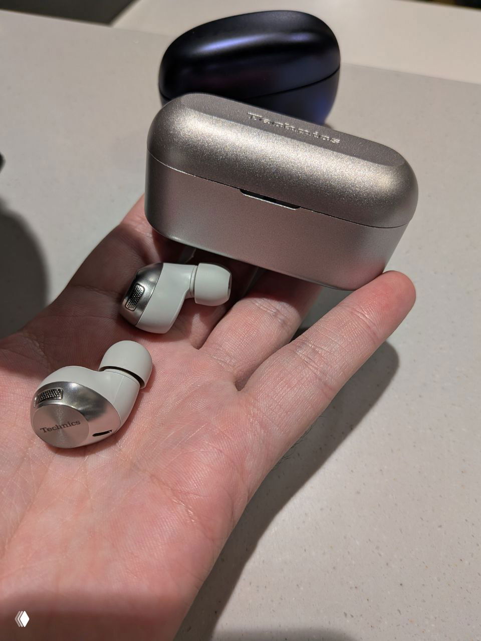 Серебристый компактный футляр и один вкладыш Technics на раскрытой ладони, крупный план формы и отделки корпуса.