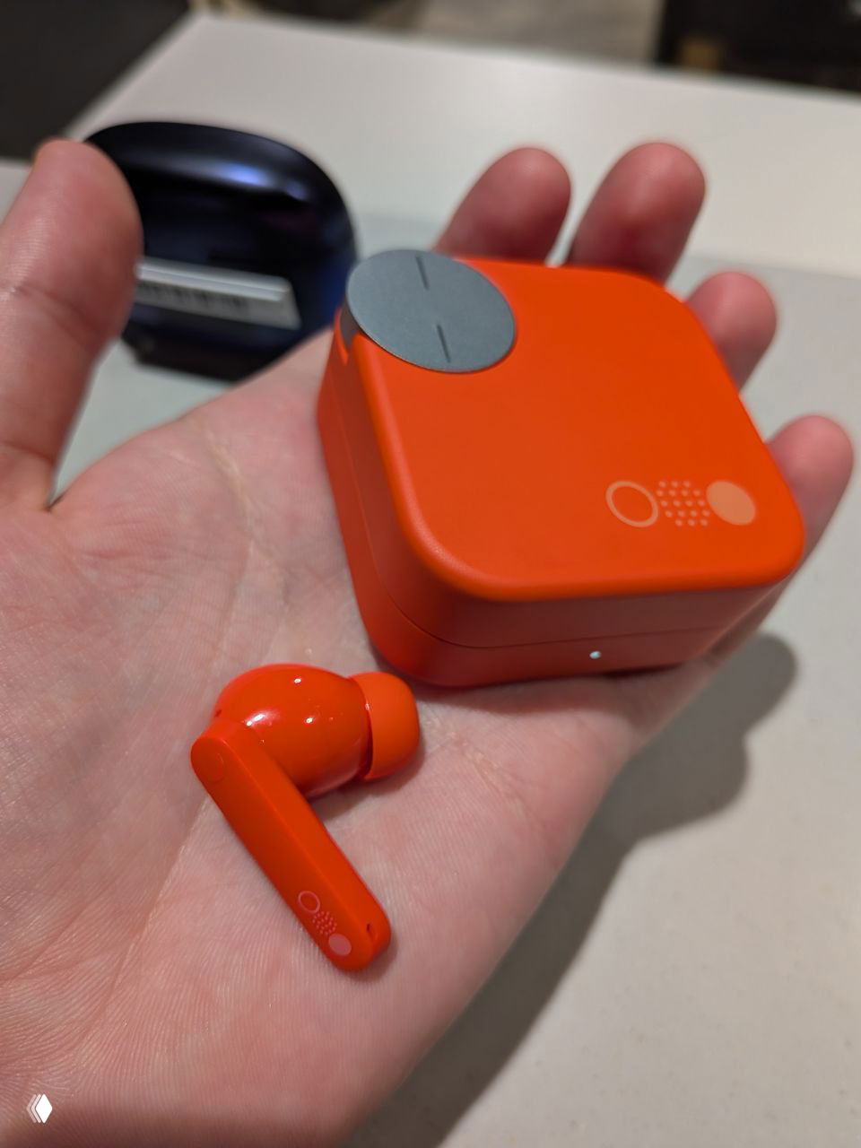 Оранжевый квадратный футляр и яркий оранжевый вкладыш на ладони — минималистичный дизайн и контрастный корпус в магазине.