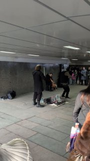 Уличные музыканты в подземном переходе: двое играют на акустических инструментах, прохожие наблюдают, урбанистическая сцена.