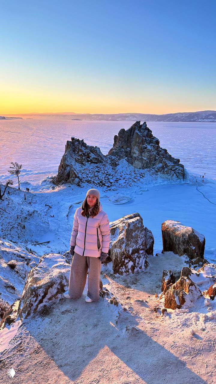 Рассвет у скалы Шаманки на фоне замёрзшего Байкала: человек на переднем плане смотрит на обширную ледяную поверхность и небо.