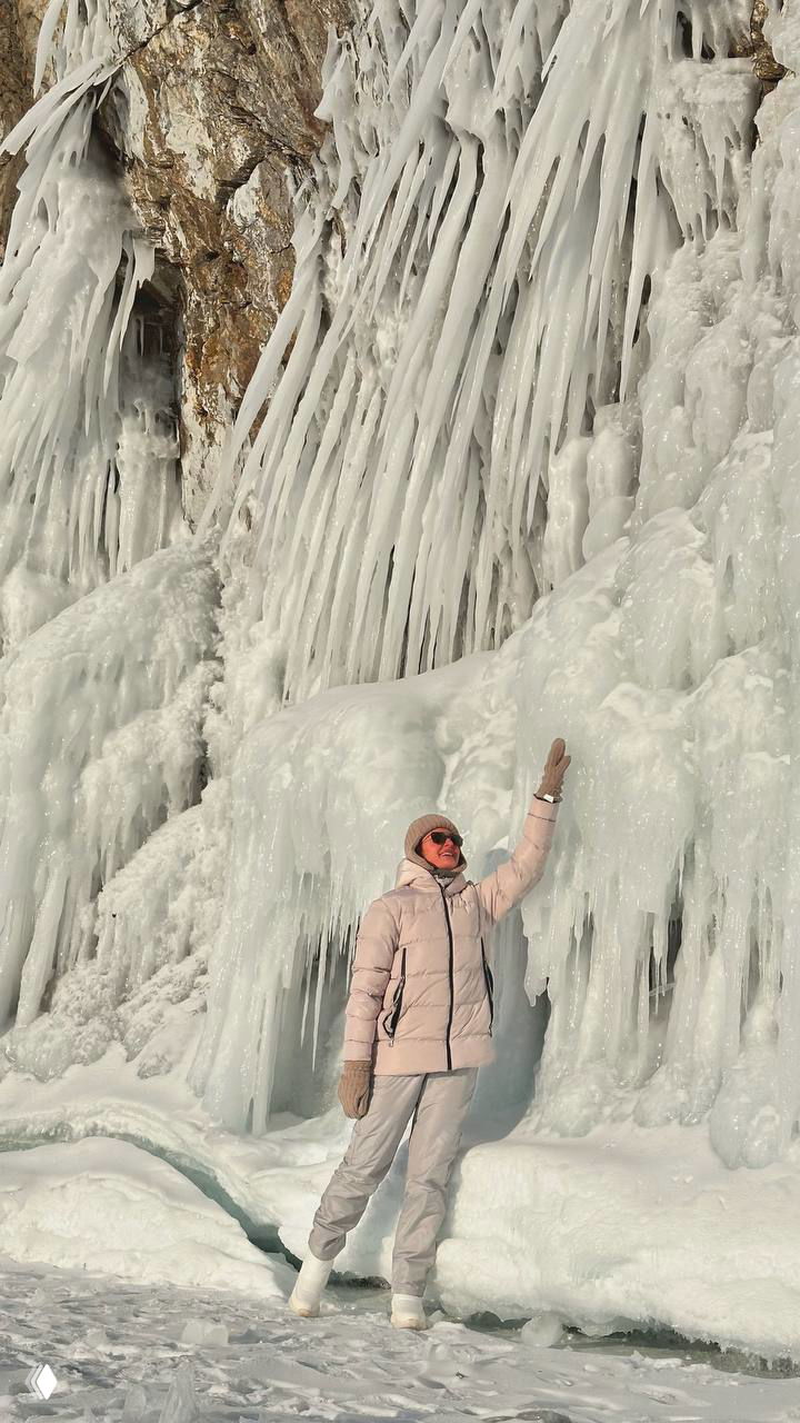 Человек на фоне причудливых ледяных колонн и сталактитов у скал — масштабные замёрзшие формы и атмосферный свет зимнего дня.
