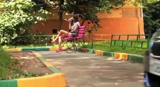 Дворовая сцена: женщина в шортах сидит на скамейке, держит телефон, рядом бордюры и зелёная трава; уличная обстановка, контекст звонка.