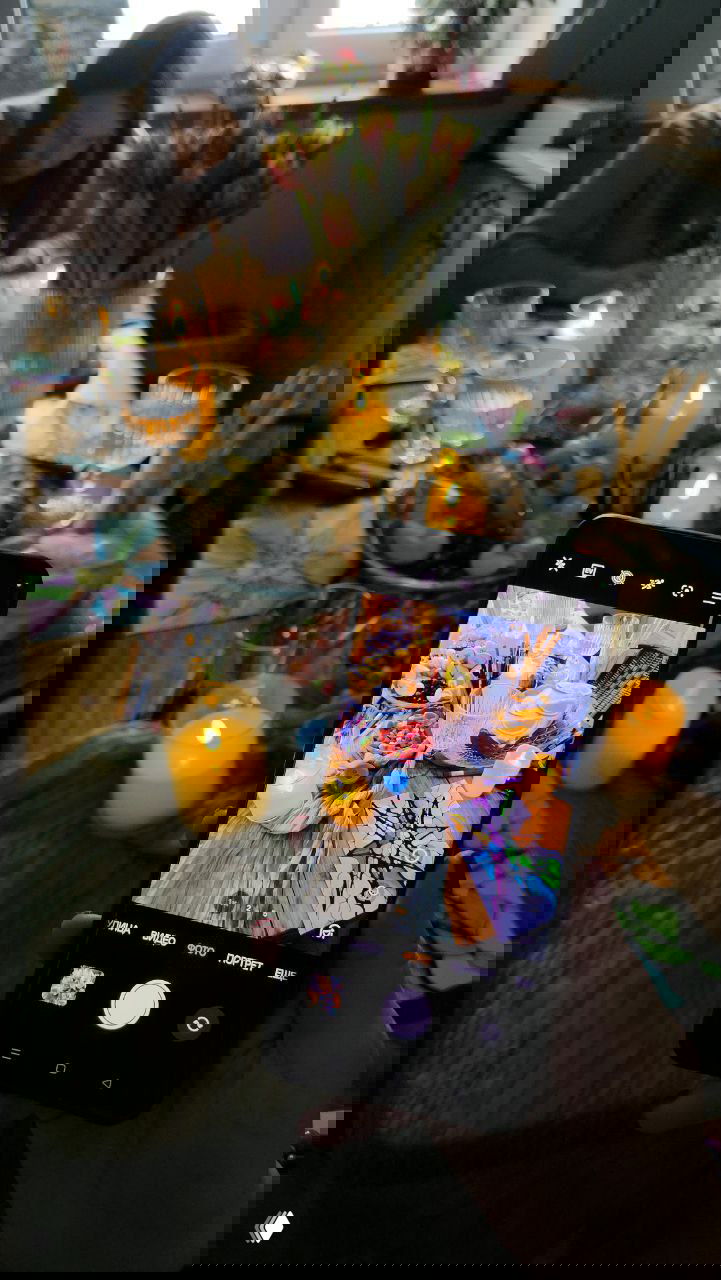 Рука держит смартфон, на экране которого кадр праздничного стола с нейрографикой, свечами и угощениями — фото процесса мастерской.