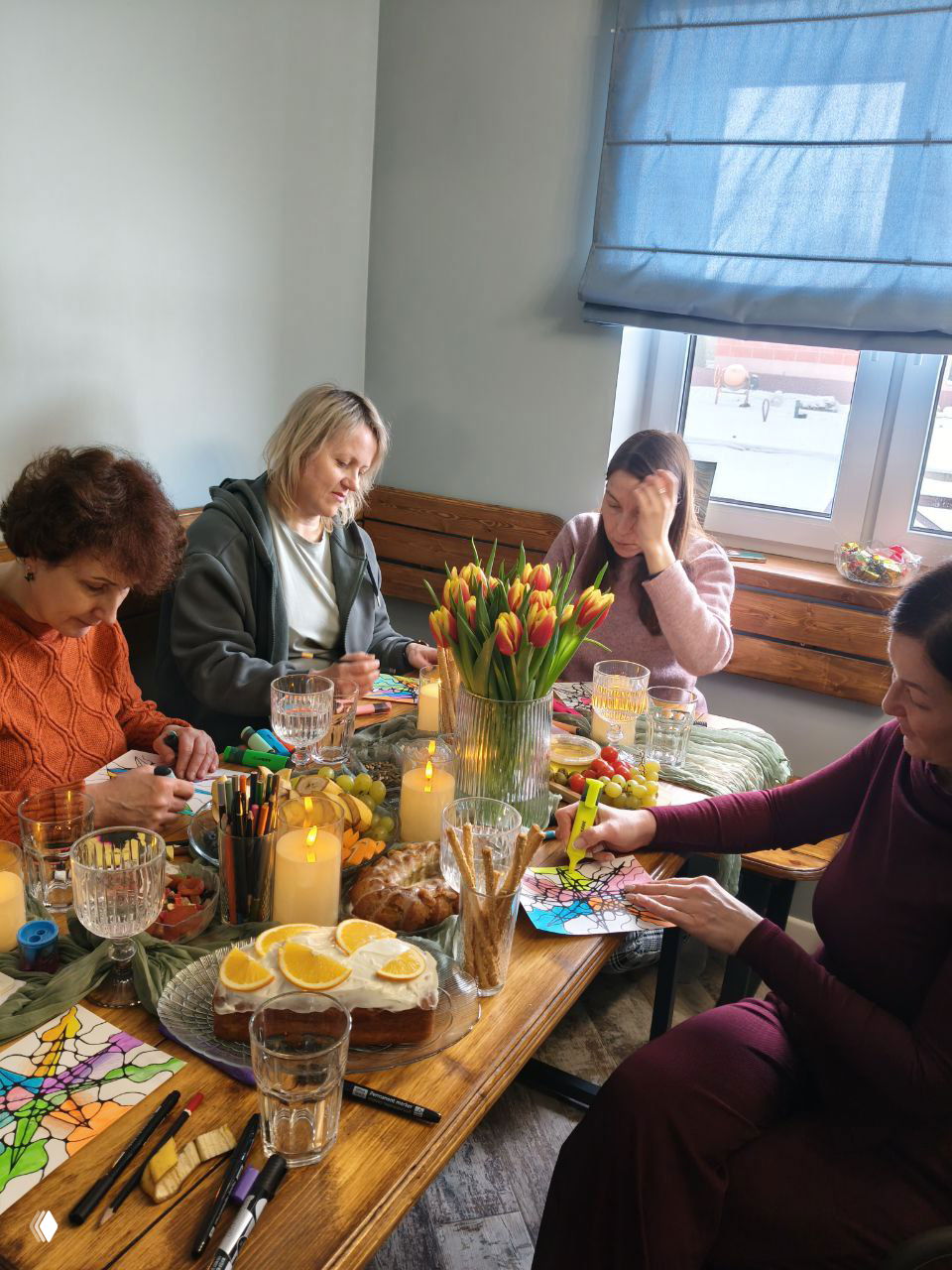 Группа участниц за столом, рисуют нейрографику, вокруг свечи и угощения — атмосферный момент банного ретрита.