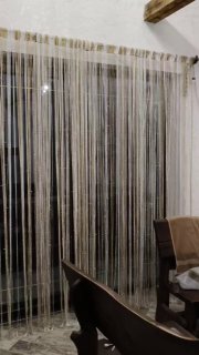 Декоративные нитяные шторки на окне в комнате отдыха бани, видно часть стола и лавок — элемент уюта в интерьере для гостей.