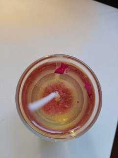 Вид сверху на декоративную свечу в стеклянном сосуде с блёстками и лепестками, снятая в бытовом интерьере — иллюстрация запускающего действия после творчества.