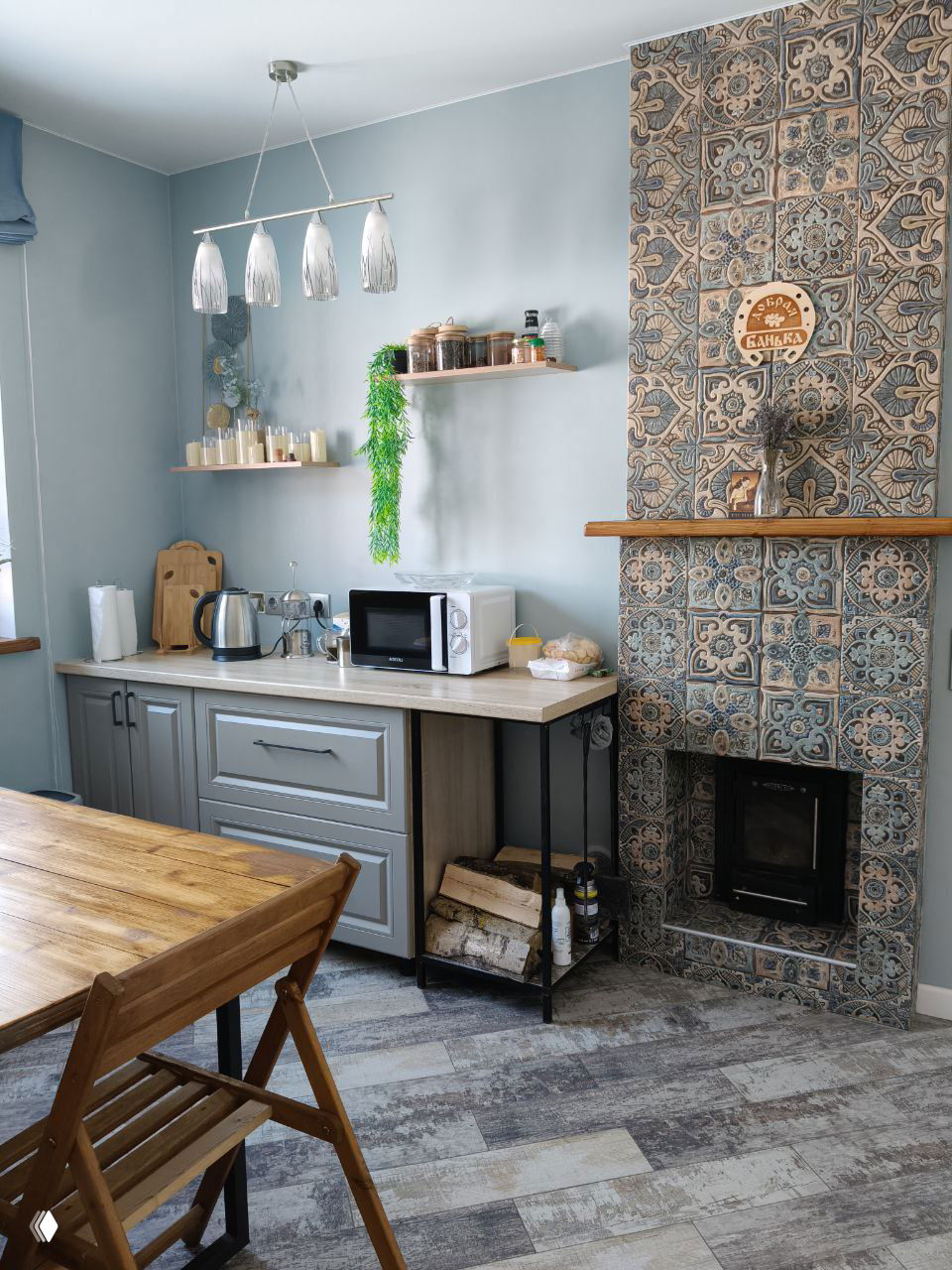 Кухонная зона и столовая возле бани: голубые стены, узорчатая плитка вокруг каминного портала, стол и подготовленное пространство для угощений.