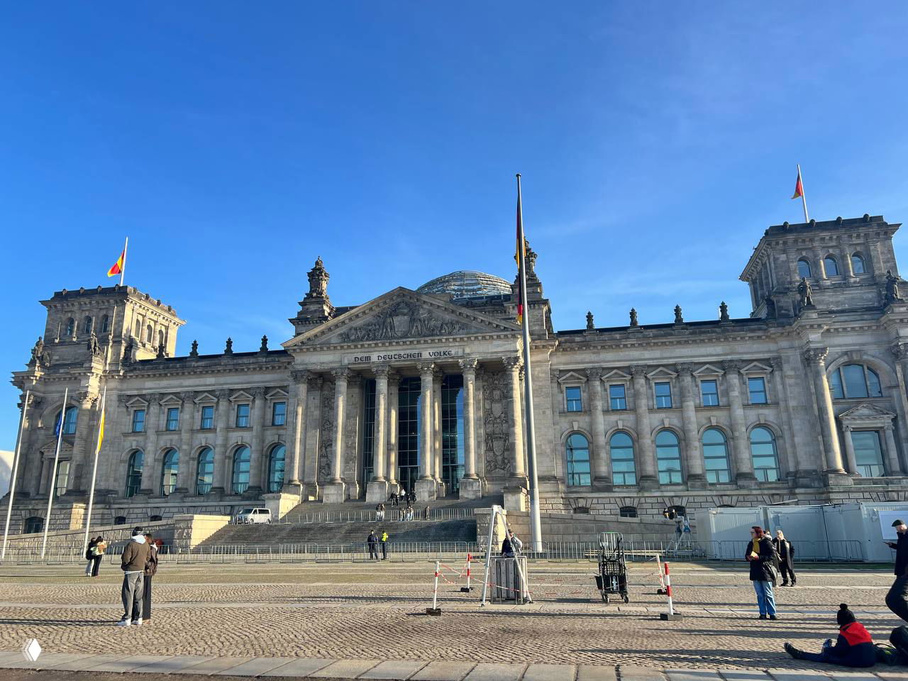 Здание Рейхстага в Берлине с куполом и флагами на фоне ясного голубого неба, архитектурный и исторический символ города.