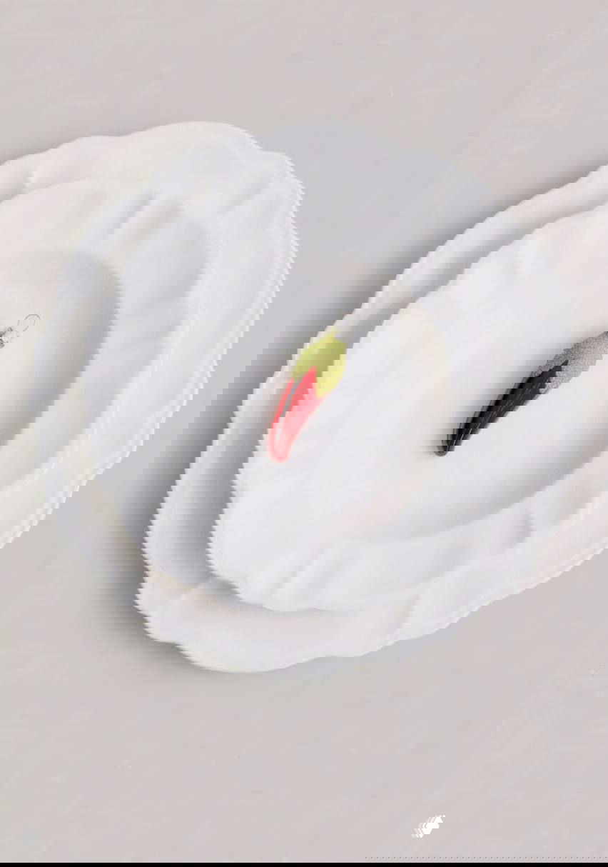 Миниатюрная игрушка-перец чили из стекла и бисера, расположена в центре белых тарелок, минималистичная студийная подача.