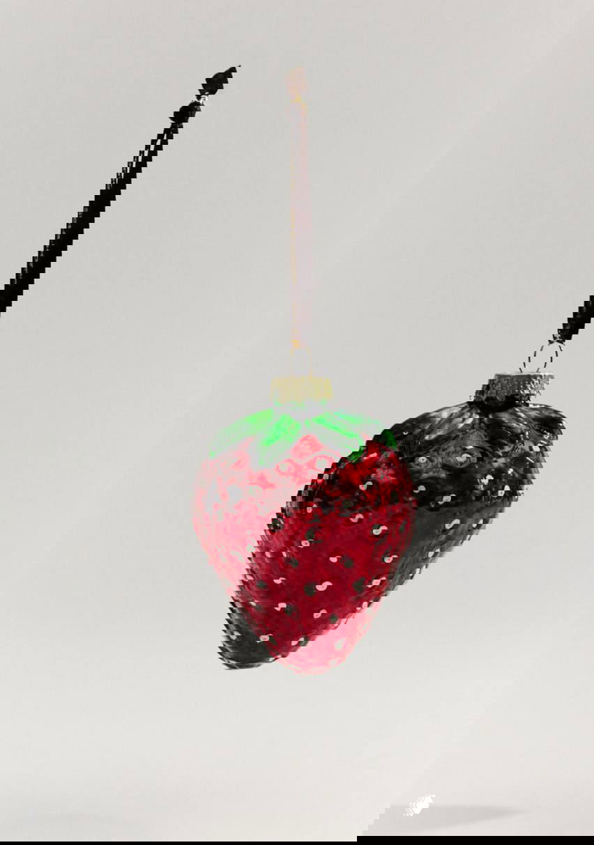 Стеклянная ёлочная игрушка в виде клубники с зелёной верхушкой и блёстками, подвешена на тёмной ленточке — студийный снимок.