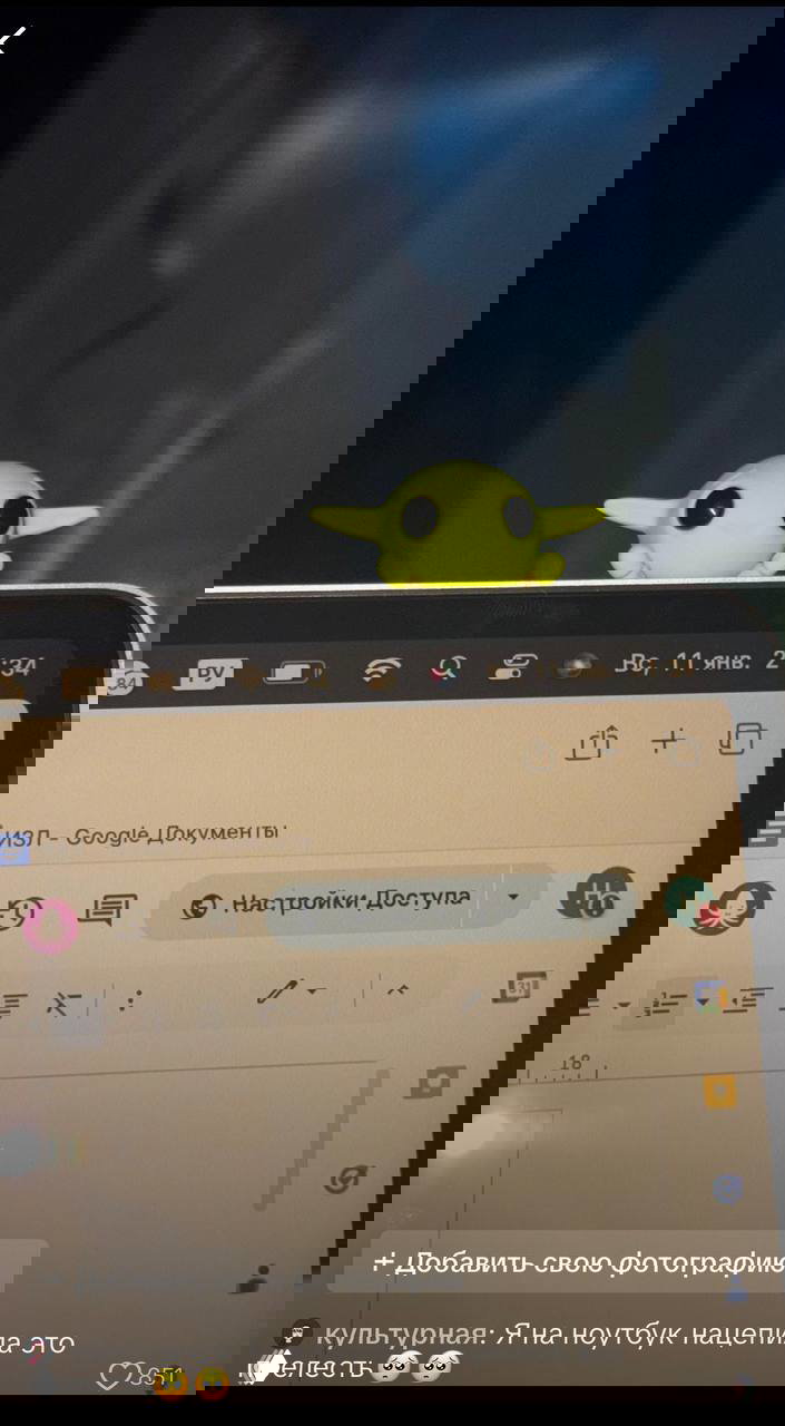 Неоново‑зеленый игрушечный эльф на верхнем краю ноутбука, на экране видны элементы интерфейса и Google Документы.