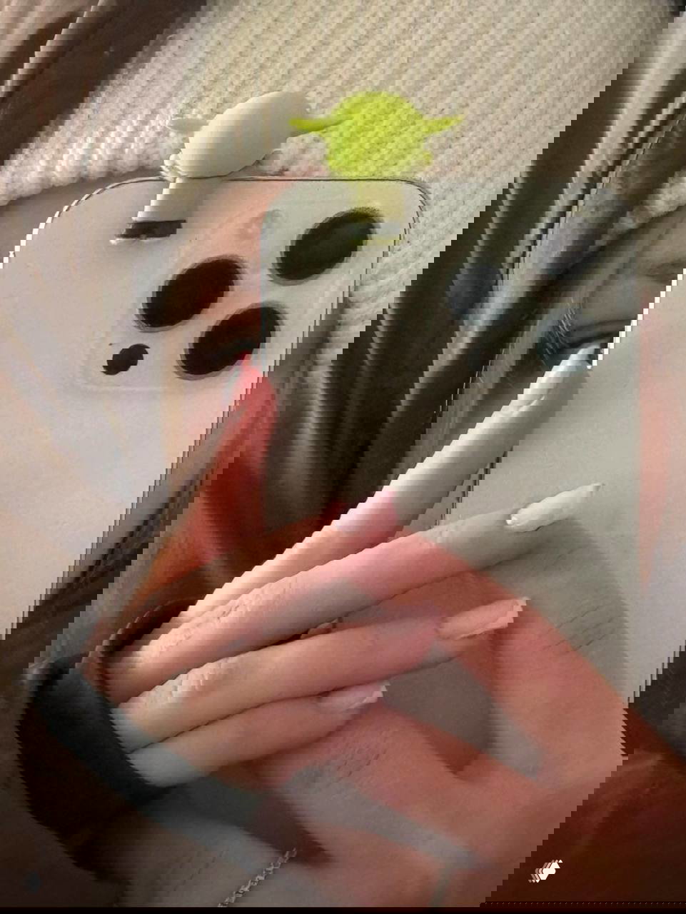 Милый зеленый эльф, прикрепленный к верхней части смартфона: селфи девушки с аксессуаром на телефоне.