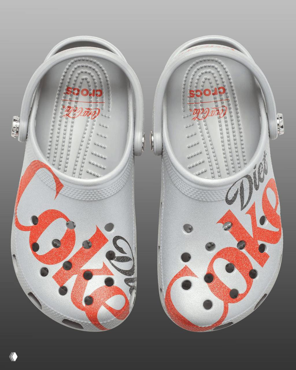 Вид сверху на серебристые клогги Diet Coke: обе туфли, отпечаток логотипа внутри и крупный принт Diet Coke на носочной части, студийная подсветка.