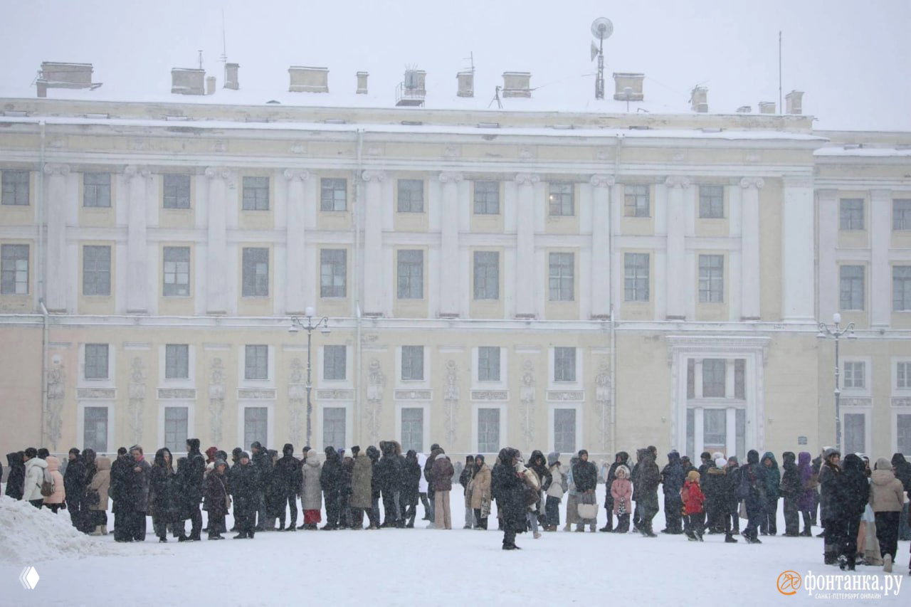 Очередь вдоль фасада Эрмитажа: группа посетителей на фоне классического здания и покрытой снегом площади, наблюдается активный снегопад.