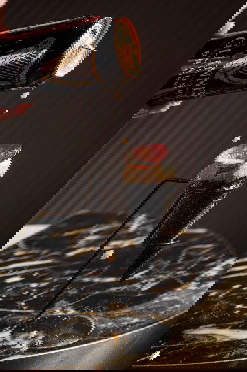 Банка Guinness льёт пенный налив на шарик пивного мороженого в тёмном вафельном рожке на подставке на мраморной поверхности.