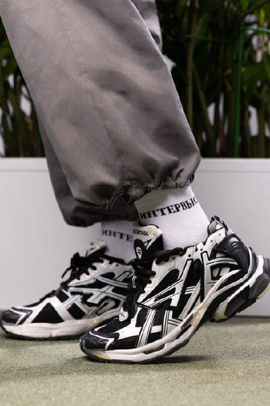 Крупный план спортивной обуви и нижней части образа на промо‑фото: кроссовки в чёрно‑белой гамме как часть образа коллекции