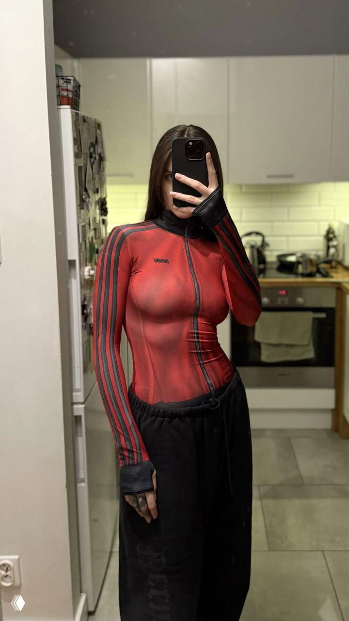 Девушка в красном и чёрном облегающем топе AVAVAV фотографирует себя в зеркале; вид в полный рост, показ посадки изделия на фигуре.