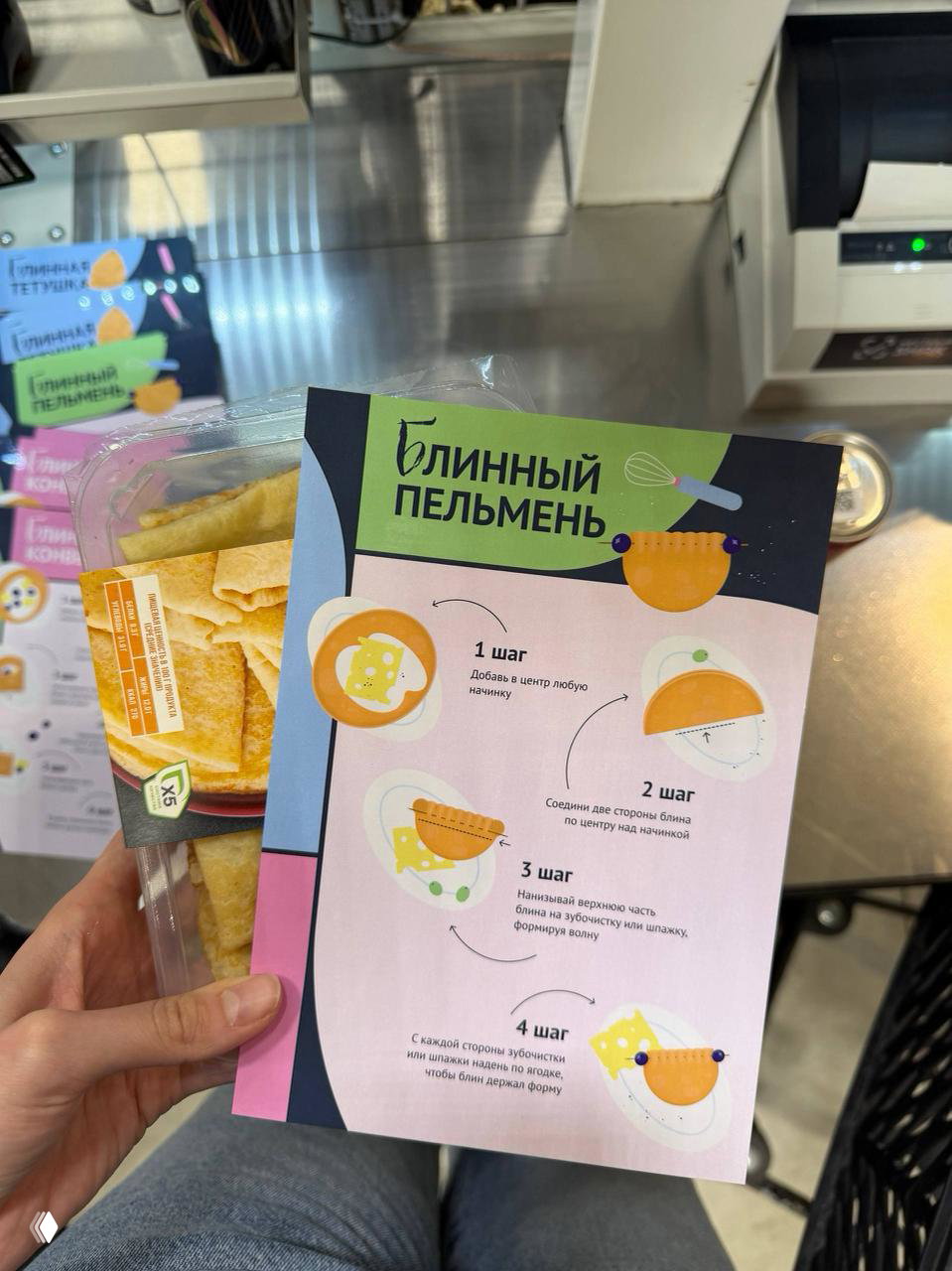 Рука держит карточку-инструкцию «Блинный пельмень» с пошаговыми иллюстрациями: 1 шаг — добавь начинку, 2 шаг — сложи стороны, 3–4 шаги — формирование и закрепление.