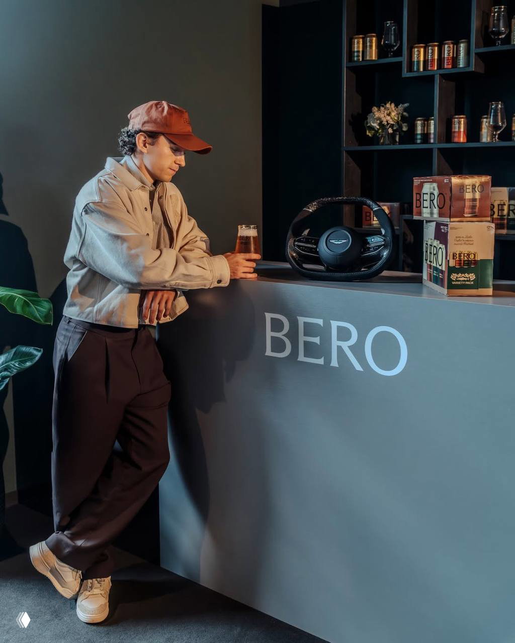 Том Холланд у стойки с логотипом BERO, на столе банки пива и рулевое колесо Aston Martin — сценография бренд‑коллаба.