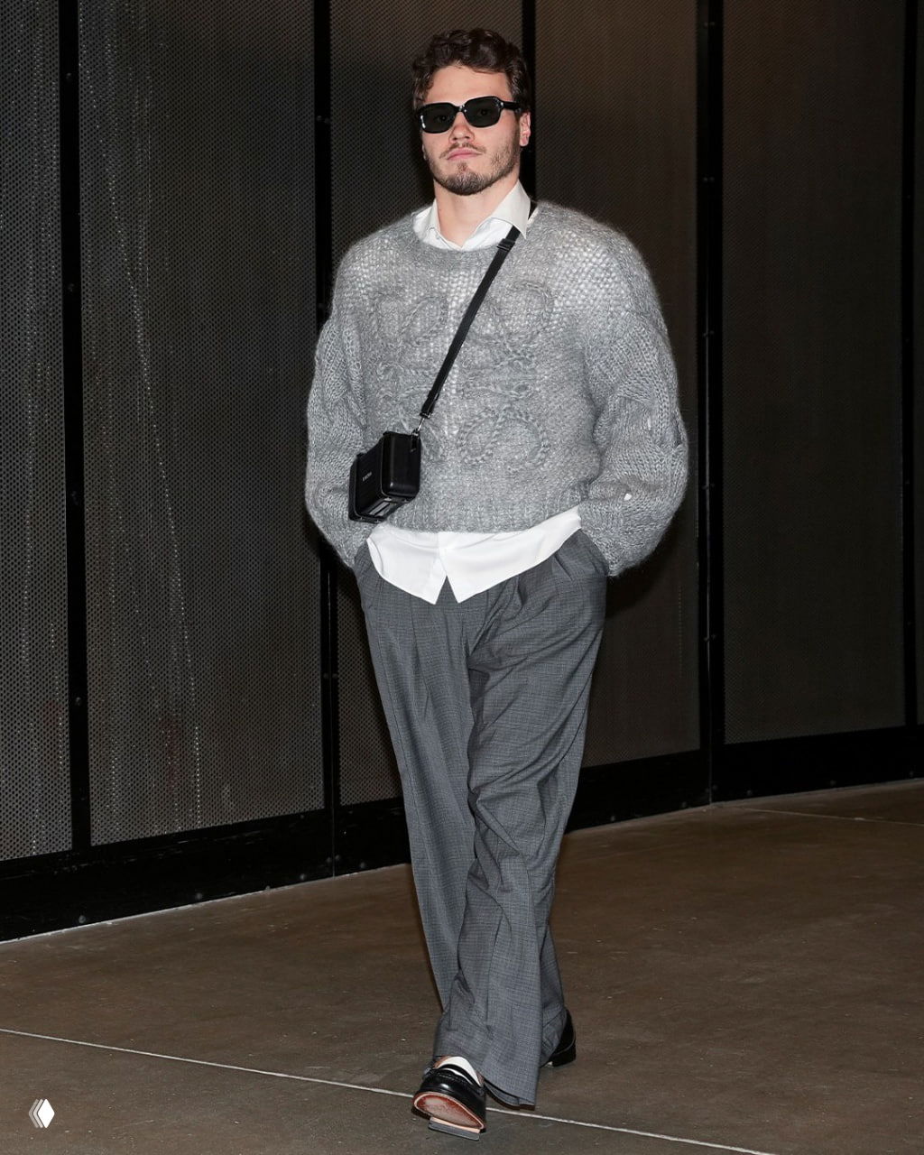 Мужчина в сером пушистом свитере и белой рубашке с маленькой сумкой через плечо идёт по коридору арены в тёмных очках, подчёркнутый лук.