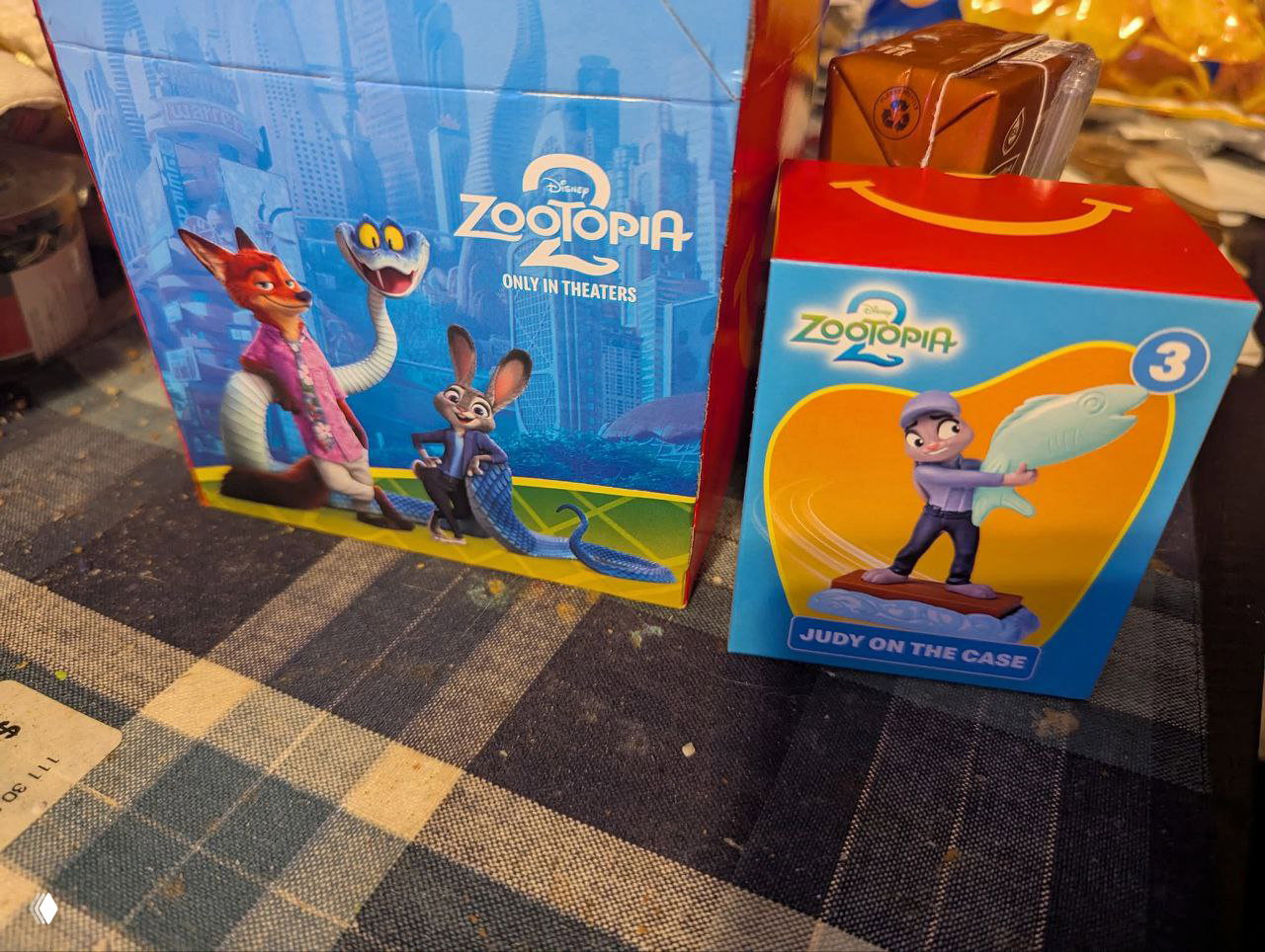 Коробки Хэппи Мил и упаковка с фигуркой «Judy on the case» на столе, видны фирменные рисунки и брендинг Zootopia 2.