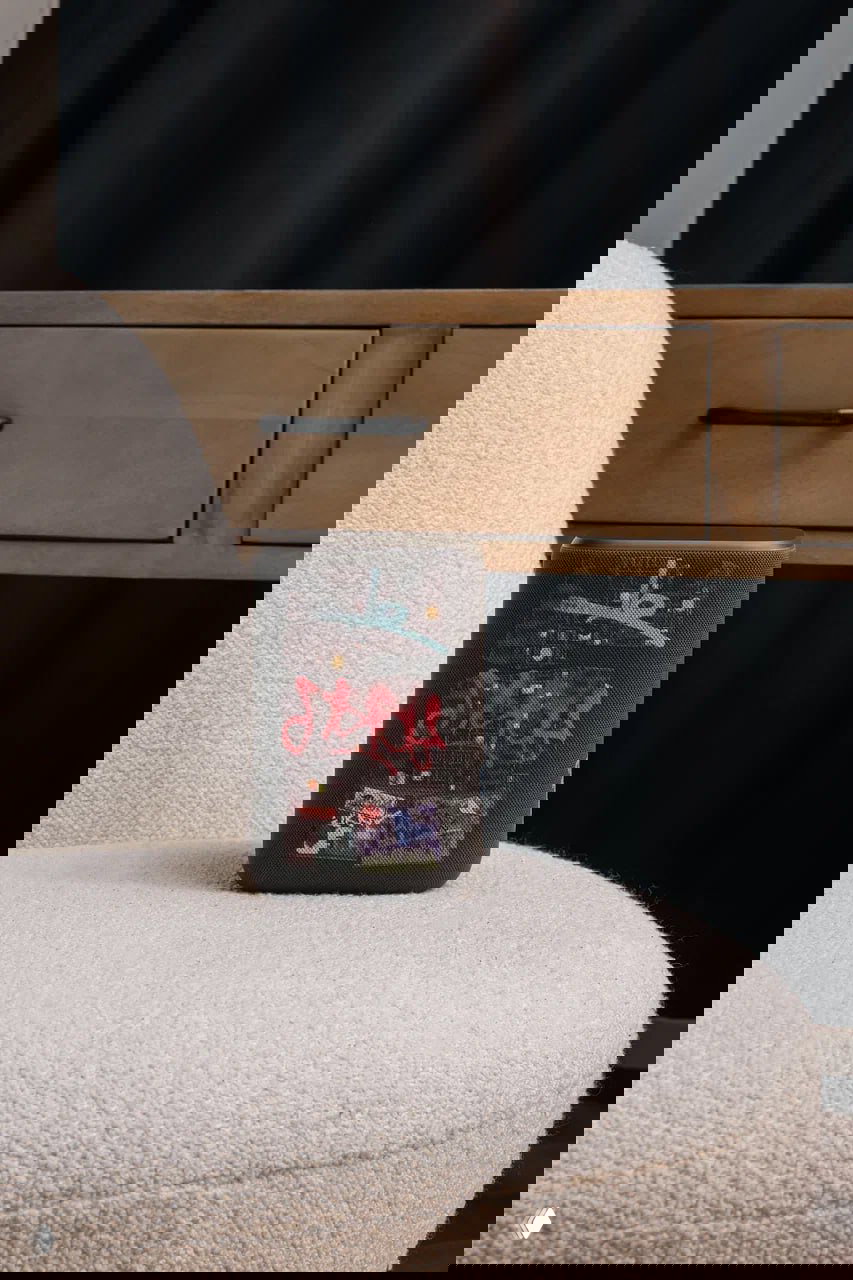 Тёмная Яндекс Станция 3 с наклейками и уличной эстетикой, стоит на мягком кресле перед деревянным комодом в домашней обстановке.