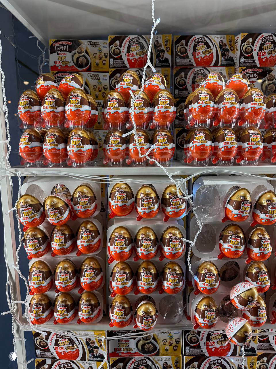 Полки магазина, уставленные упаковками Kinder Joy Harry Potter: многочисленные шоколадные яйца в блистерах на витрине.