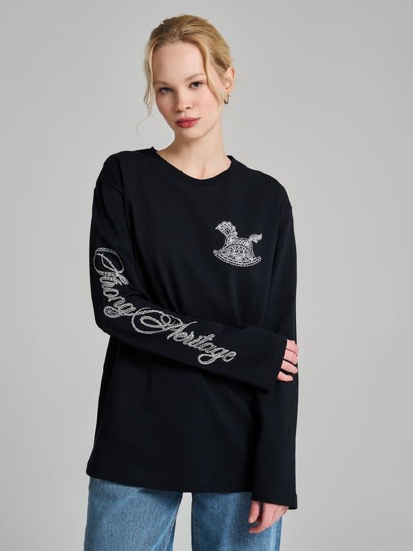 Модель в чёрном лонгсливе с вышитым или принтованным изображением коняшки-качалки и декоративной надписью на рукаве.