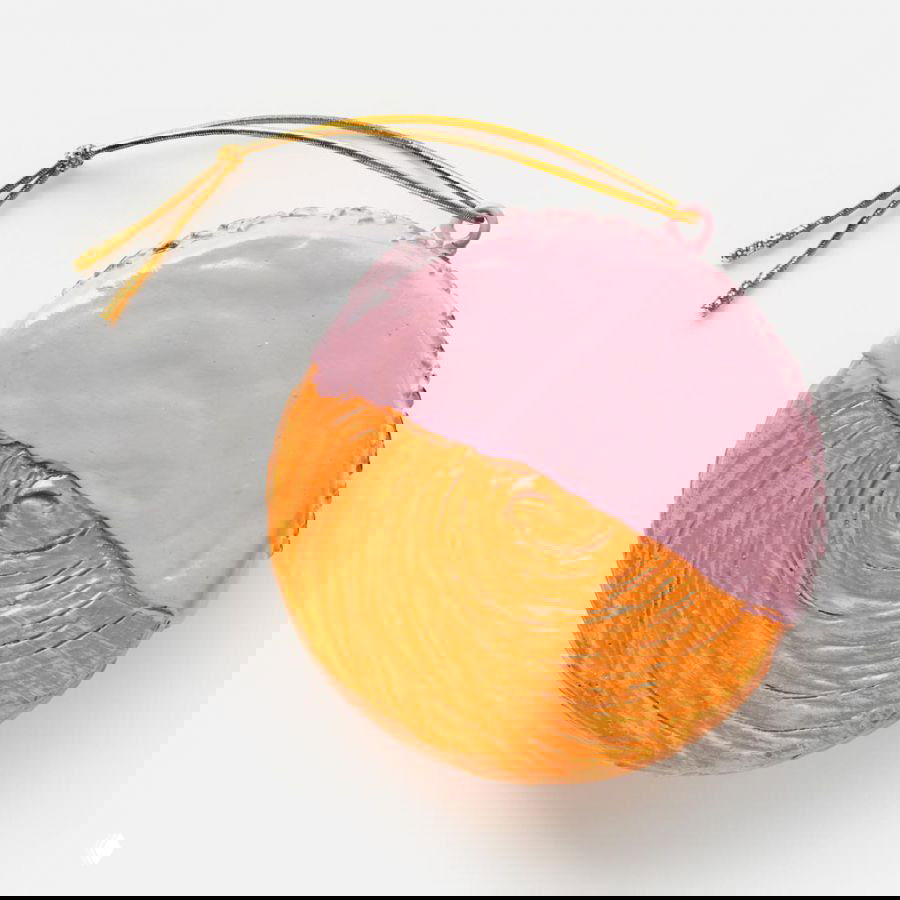 Круглая ёлочная игрушка‑плюшка с розовой глазурью на половине поверхности, с рельефной текстурой и золотым шнурком, на белом фоне.