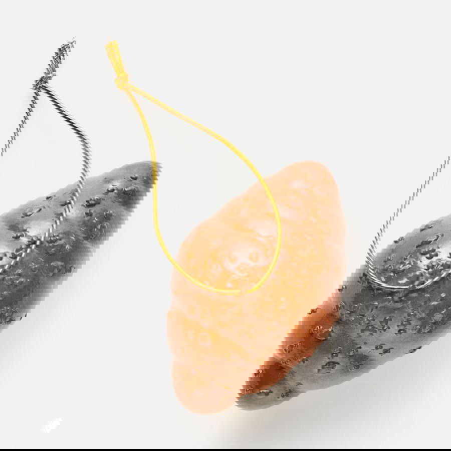 Бронзово‑коричневая ёлочная игрушка в форме круассана или булочки с текстурой и золотым шнурком, снята на белом фоне.