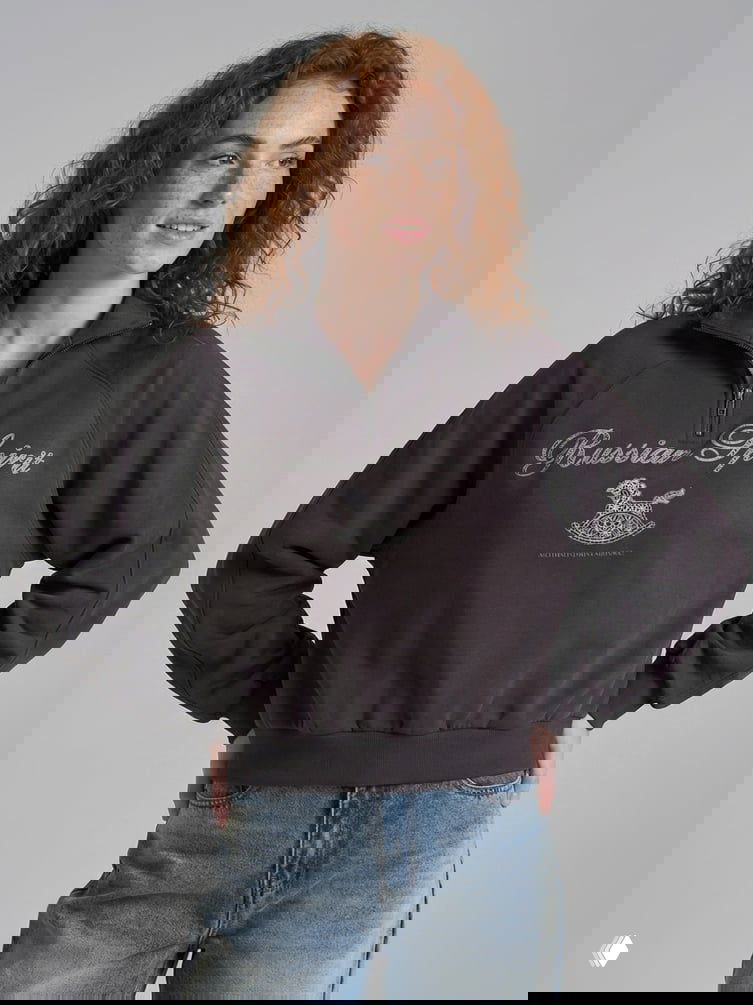 Женская модель в тёмной толстовке с надписью «Russian Spirit» и графическим изображением коняшки-качалки, студийная съёмка в нейтральном фоне.