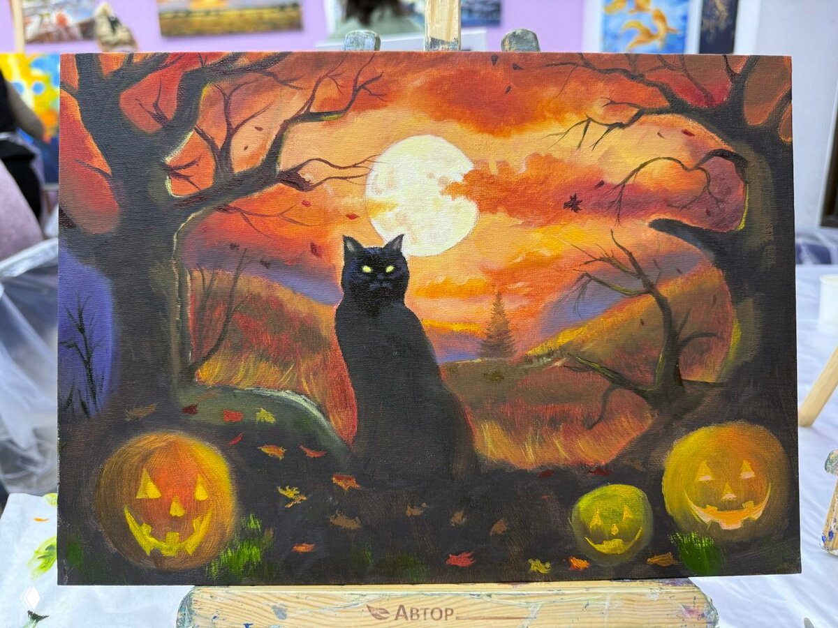 Картина в тёплых осенних тонах: чёрная кошка на фоне полной луны, тыквы-джек‑о‑лантерны и силуэты деревьев в пейзаже.