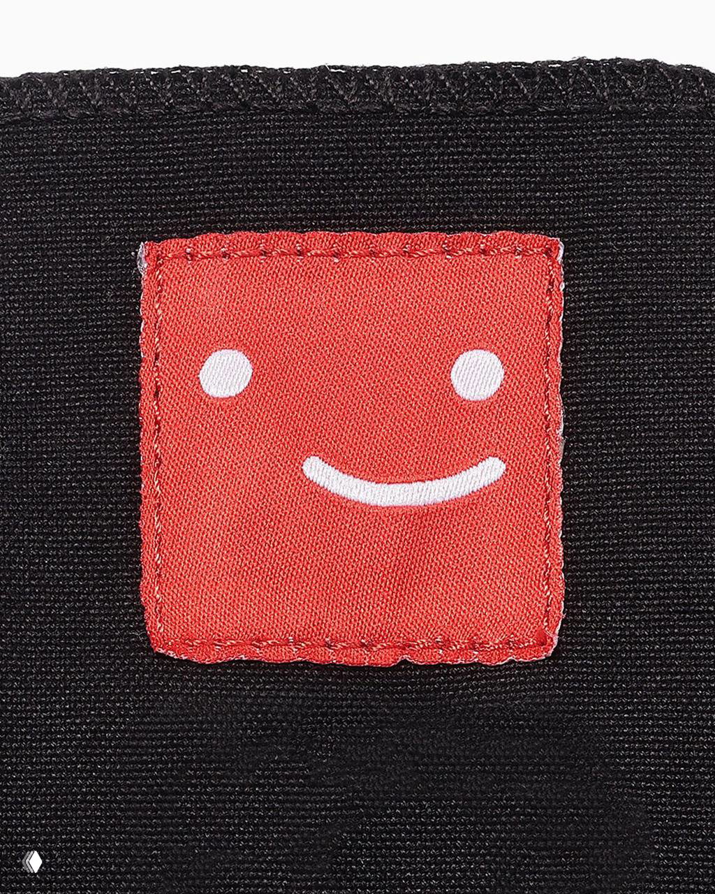 Крупный план красного нашивного квадрата с улыбающимся лицом на язычке кеды — деталь оформления коллаборации Netflix x Converse.