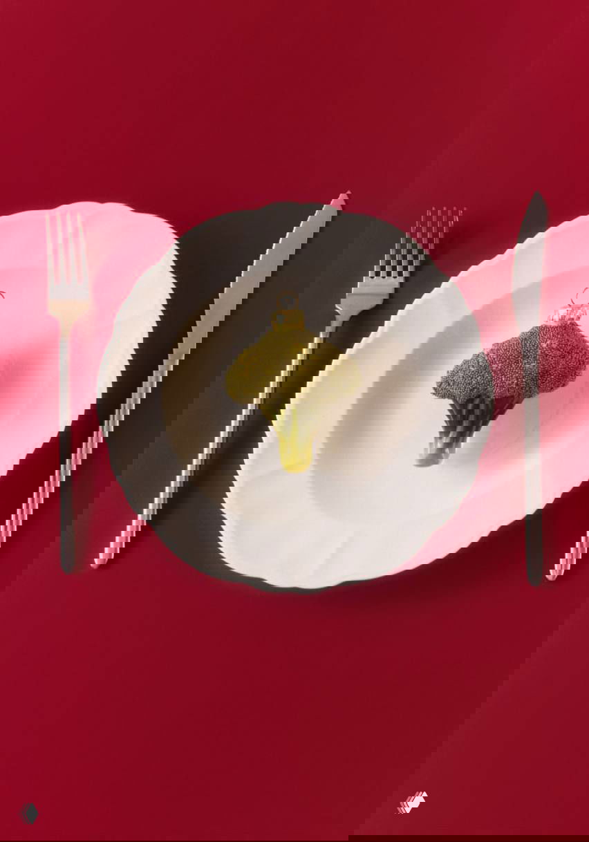 Ёлочная игрушка в виде соцветия брокколи, сделана из стекла и бисера, размещена на белой тарелке на красном фоне.